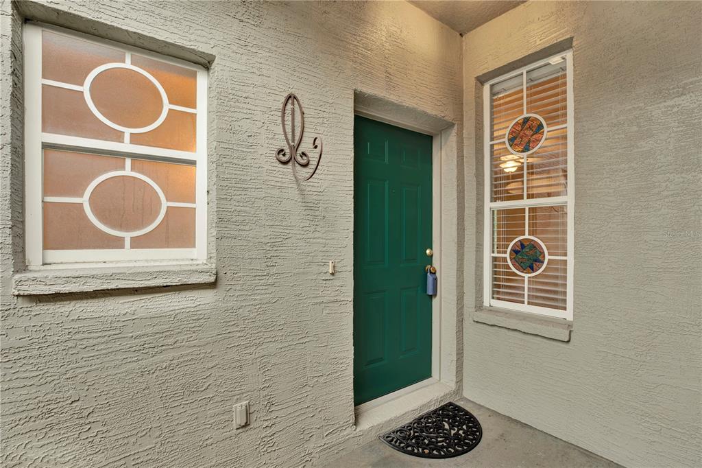 A green front door is flanked by two windows with decorative inserts on a stucco wall — 4353 BROOKER CREEK DR, PALM HARBOR, FL