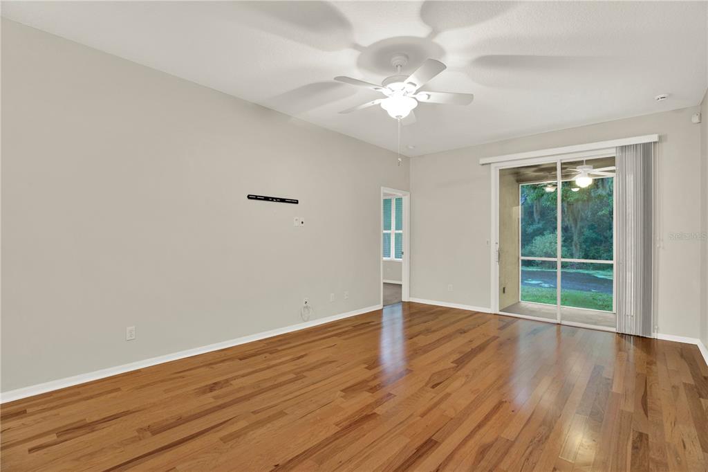 An empty living room features hardwood floors, a ceiling fan, and sliding glass patio doors — 4353 BROOKER CREEK DR, PALM HARBOR, FL