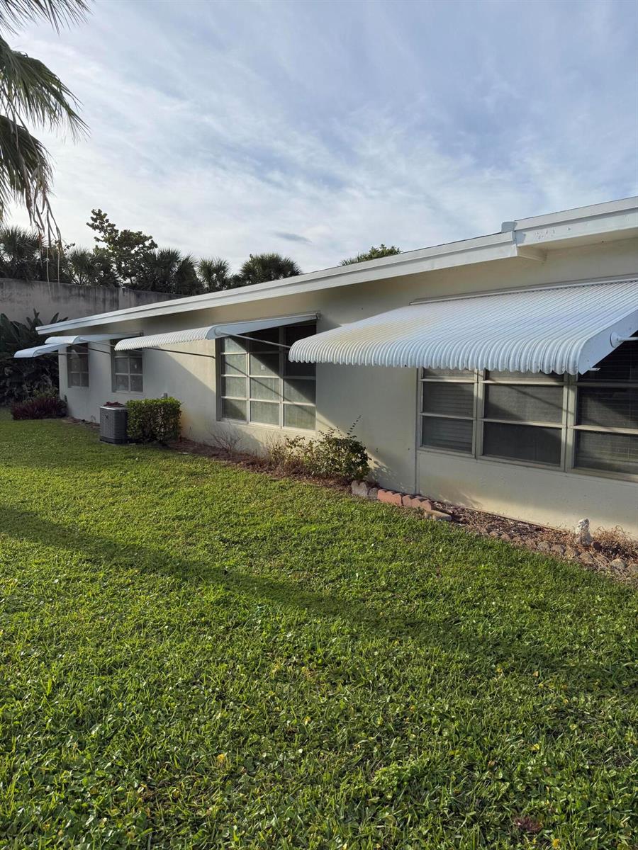 The exterior of a house features white metal awnings over several windows and a lawn — 3311 Valley Road # D, Boynton Beach FL 33435, BOYNTON BEACH, FL