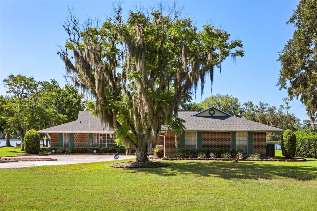 A brick ranch-style house with green shutters sits behind a large tree with Spanish moss — 6720 BAY SHORE DRIVE, ST CLOUD, FL