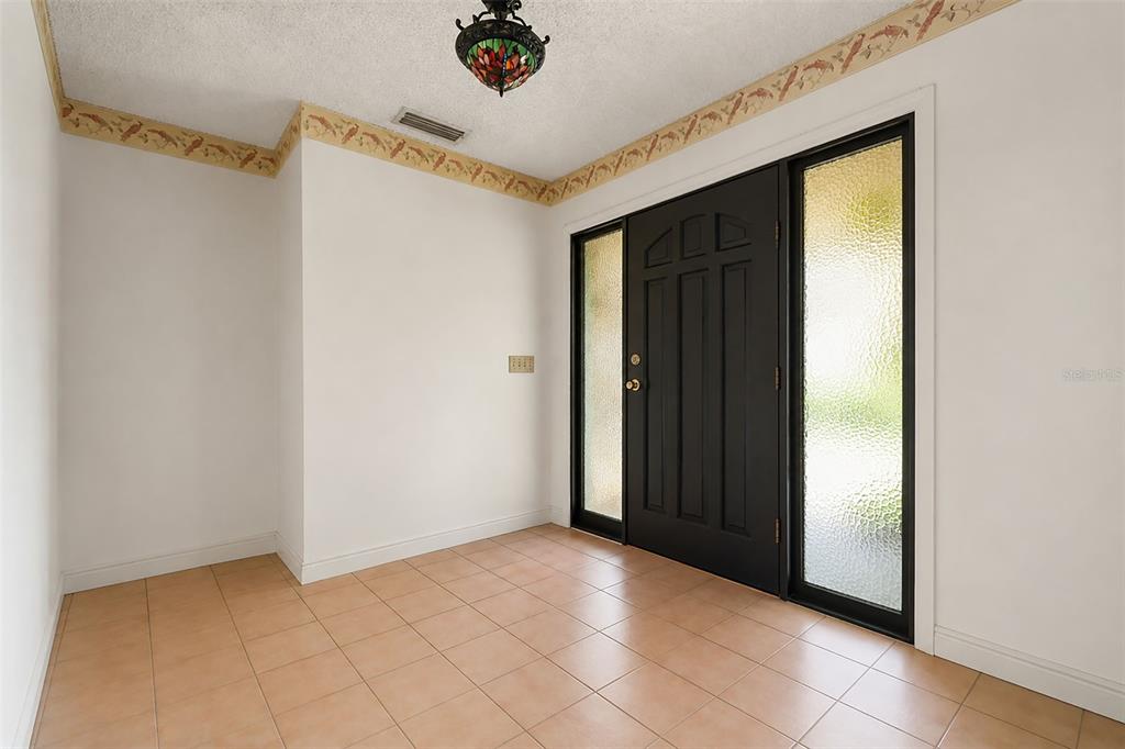 An entryway with tan tile flooring, white walls, a decorative border, and a black front door — 6720 BAY SHORE DRIVE, ST CLOUD, FL