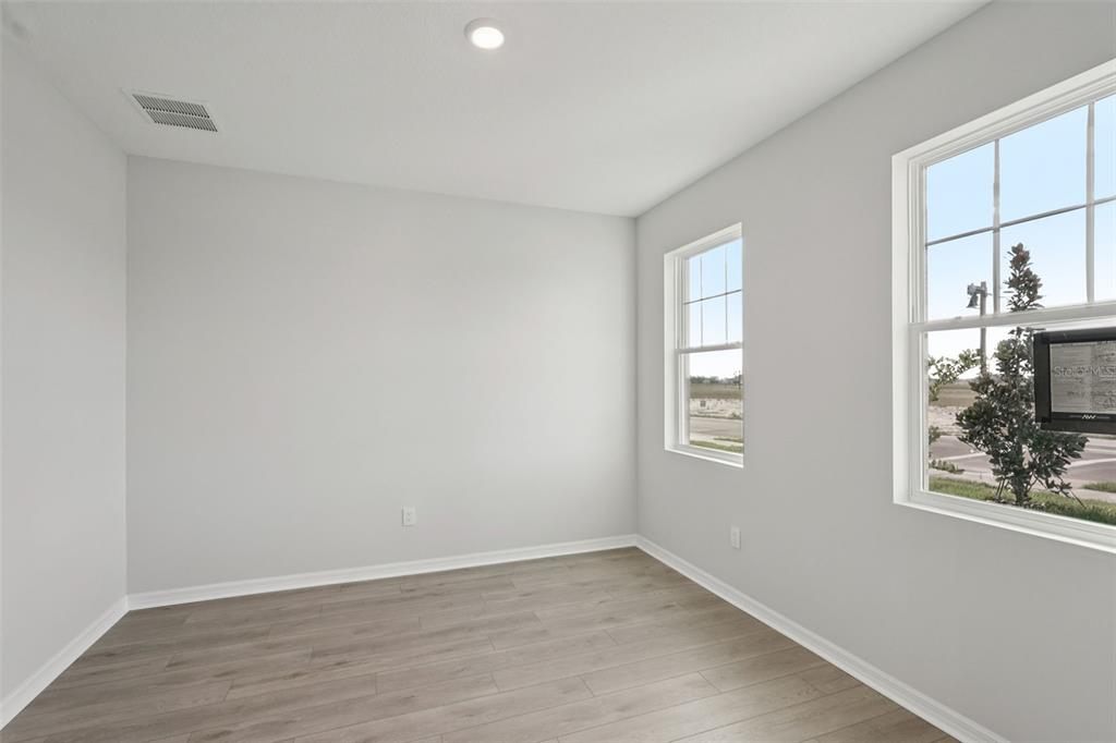 An empty room with light gray walls, wood-look flooring, and two windows overlooking a street — 2902 CITRUS GROVE STREET, WIMAUMA, FL