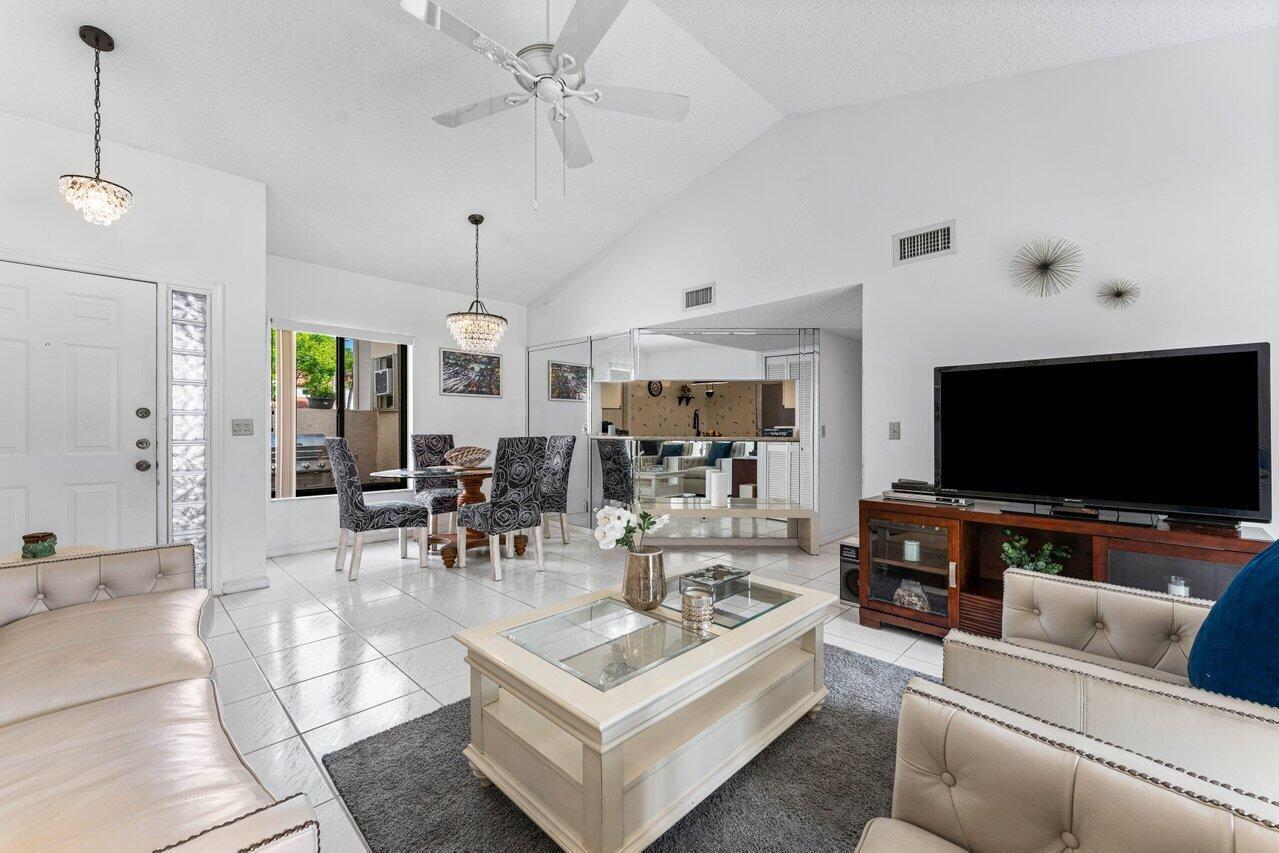 A living room with tile floors, a vaulted ceiling, and a dining area with mirrored walls — 10 Via De Casas Sur # 104, Boynton Beach FL 33426, BOYNTON BEACH, FL