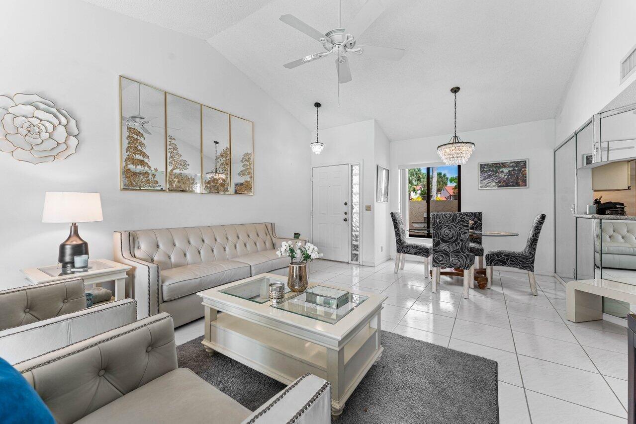 A bright living and dining area features white tile floors, a tufted sofa, and chandeliers — 10 Via De Casas Sur # 104, Boynton Beach FL 33426, BOYNTON BEACH, FL