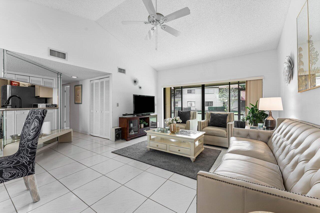 A living room features white tile floors, a tufted sofa, and a sliding glass door — 10 Via De Casas Sur # 104, Boynton Beach FL 33426, BOYNTON BEACH, FL