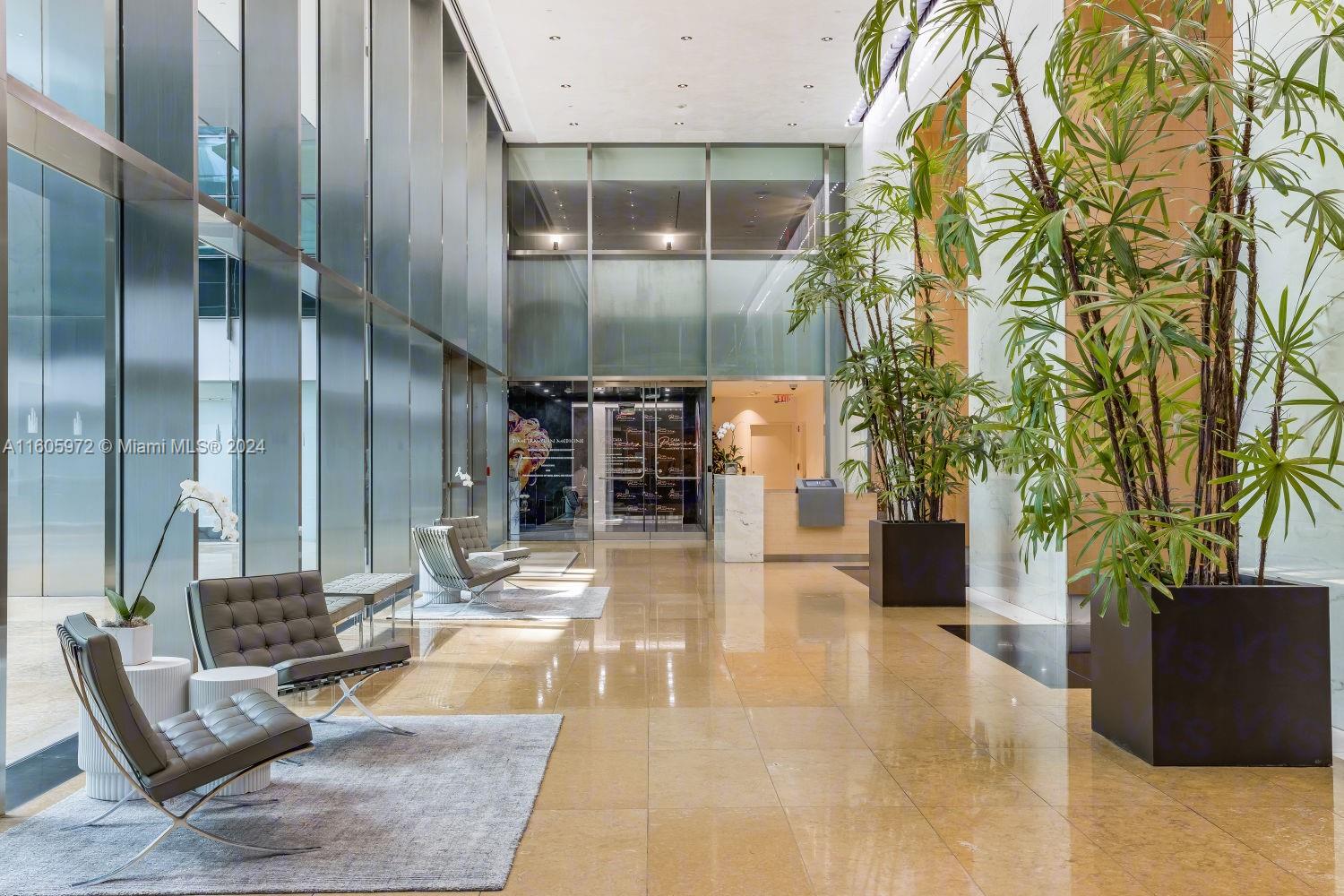 A modern building lobby features glass walls, polished tile floors, and several potted indoor plants — 1395 Brickell Ave, Miami FL 33131, MIAMI, FL