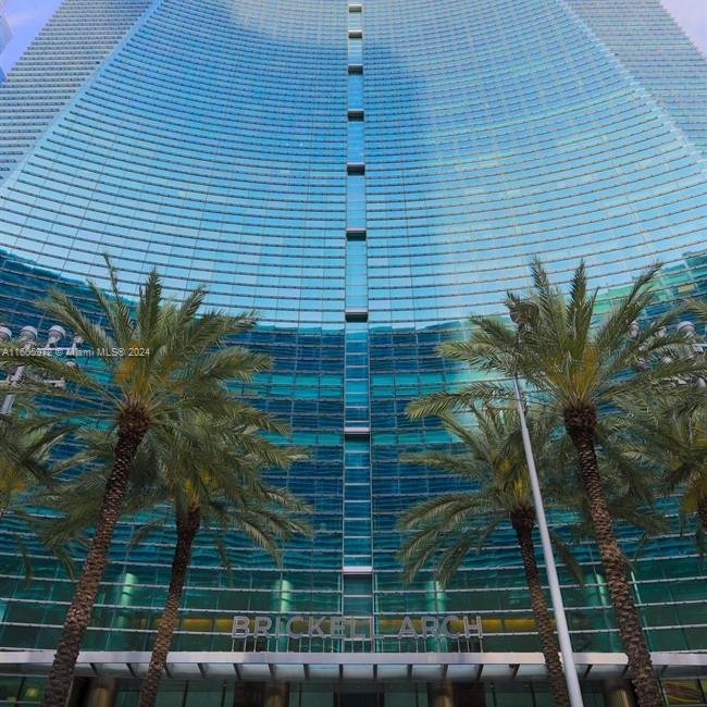 A low-angle view of the glass-facade Brickell Arch building with palm trees in the foreground — 1395 Brickell Ave, Miami FL 33131, MIAMI, FL