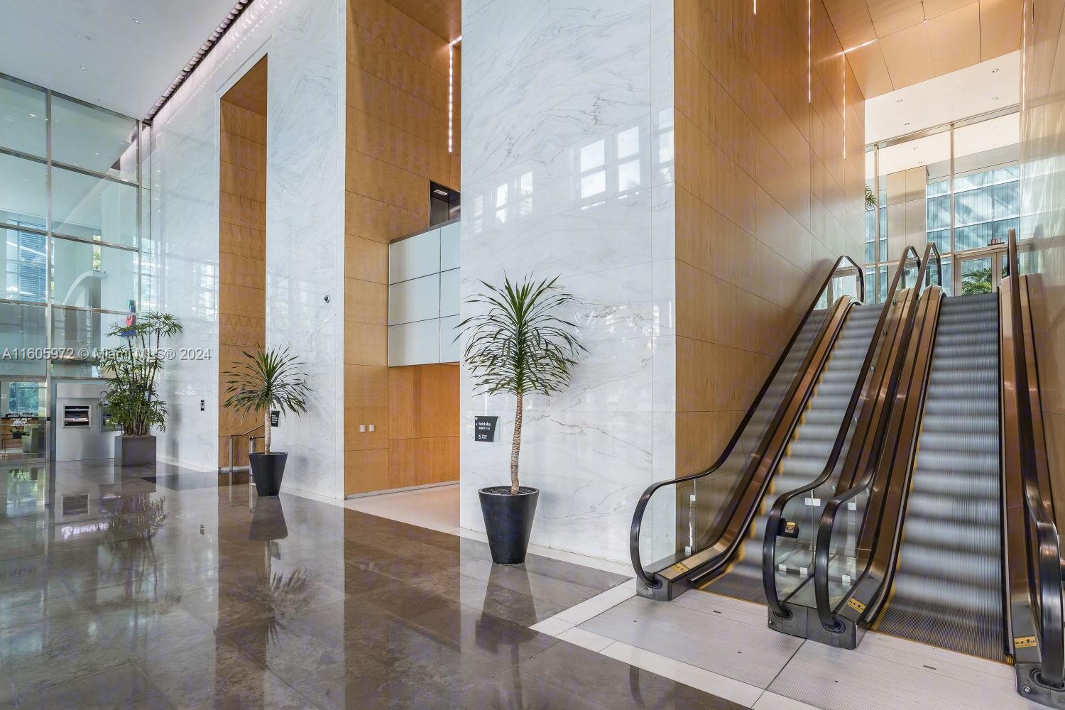 A modern lobby features marble walls, wood paneling, a polished floor, and an escalator — 1395 Brickell Ave, Miami FL 33131, MIAMI, FL