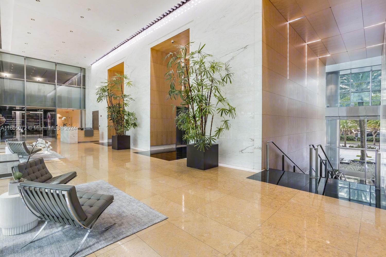 A modern building lobby features marble walls, tall potted plants, and gray lounge chairs — 1395 Brickell Ave, Miami FL 33131, MIAMI, FL