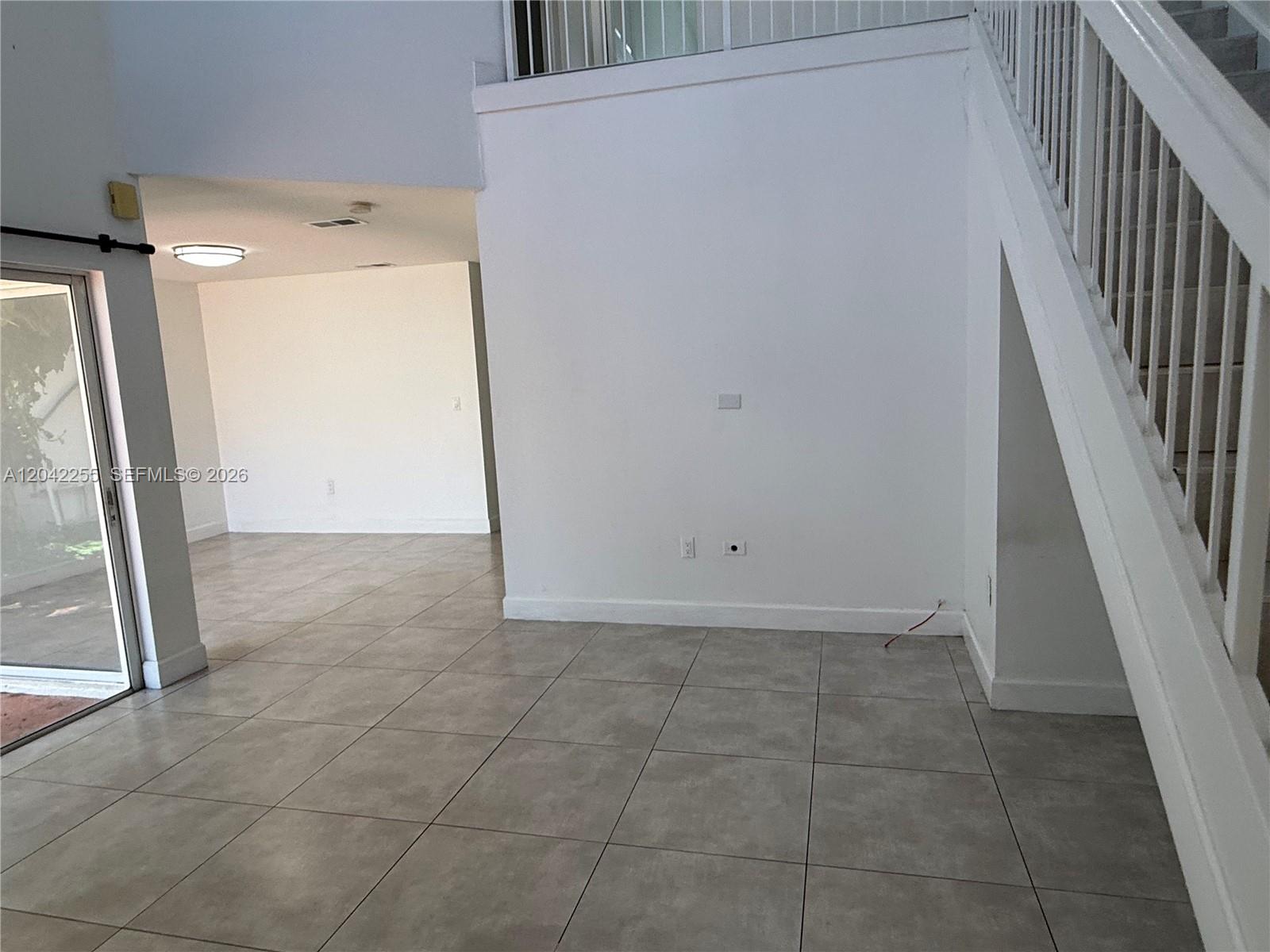 A room with large floor tiles, a staircase with white railings, and a sliding glass door — 14912 SW 104th St # 48, Miami FL 33196, MIAMI, FL