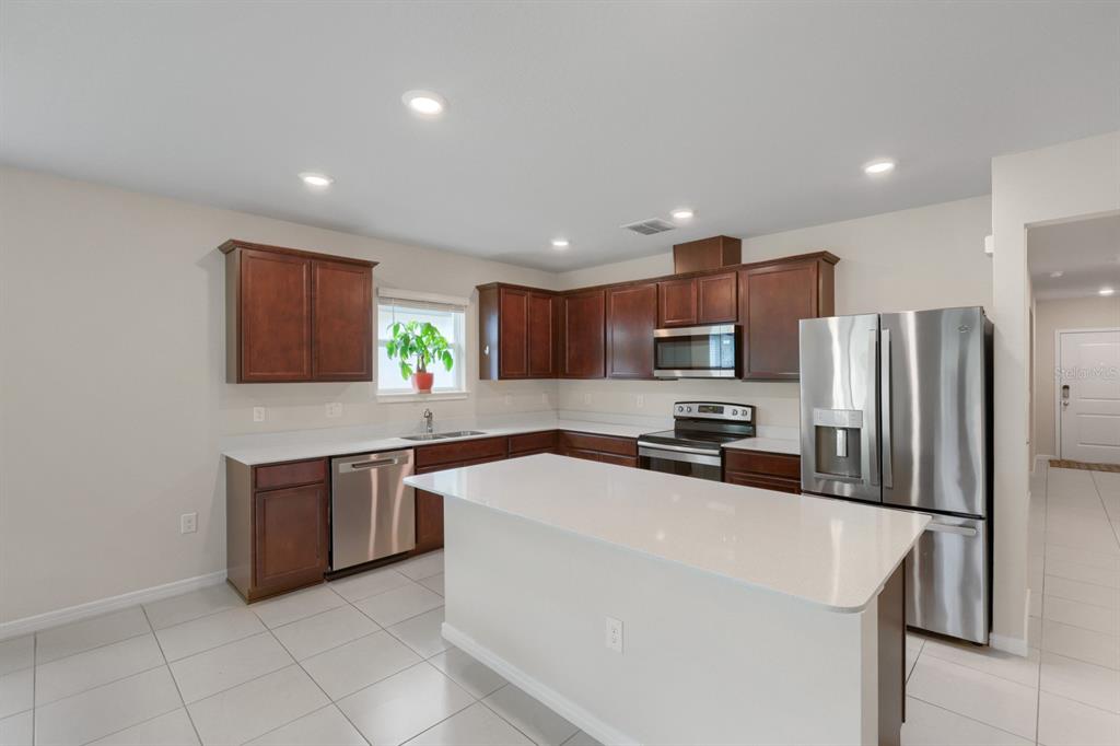 A kitchen with dark wood cabinets, stainless steel appliances, and a white quartz island — 30169 MERILEE PLACE, WESLEY CHAPEL, FL