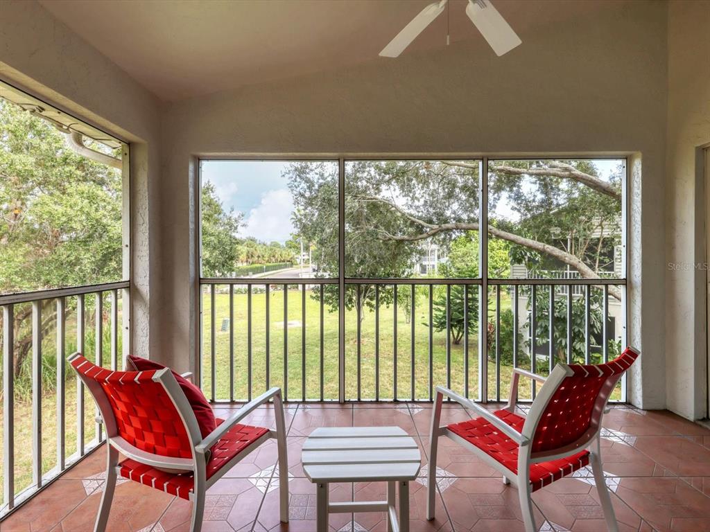 A screened-in balcony features two red chairs, a small table, and tile flooring — 7234 ELEANOR CIRCLE UNIT 203, SARASOTA, FL