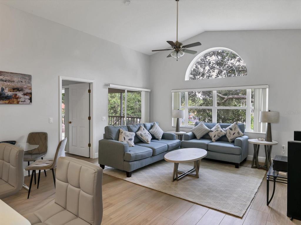 A living room features light wood floors, blue sofas, and a large arched window — 7234 ELEANOR CIRCLE UNIT 203, SARASOTA, FL