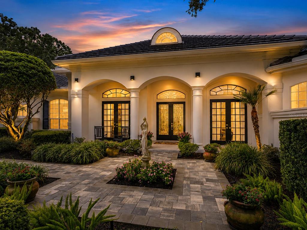 A single-story house with arched entryways, a paved courtyard, and a central statue at dusk — 9004 GREAT HERON CIRCLE, ORLANDO, FL