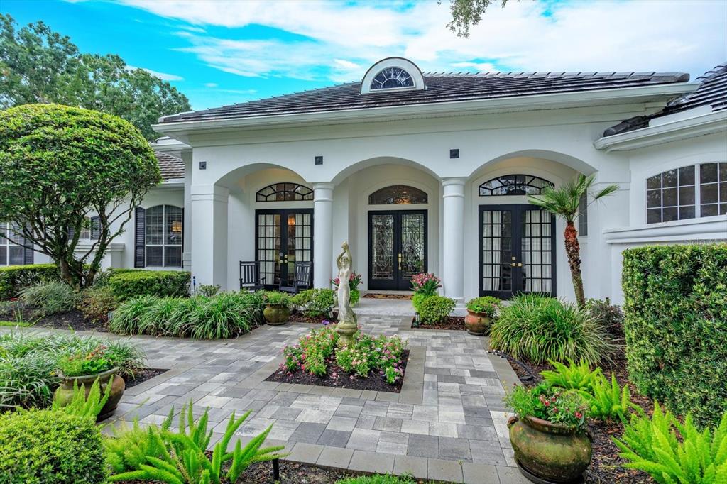 A white house exterior features a stone-paved walkway, arched entryways, and a central garden statue — 9004 GREAT HERON CIRCLE, ORLANDO, FL