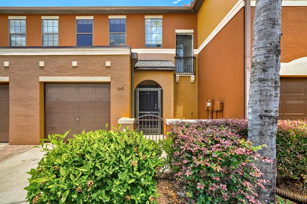 A two-story townhouse exterior with a garage, front entrance, and a small balcony — 1048 TULLAMORE DRIVE, WESLEY CHAPEL, FL