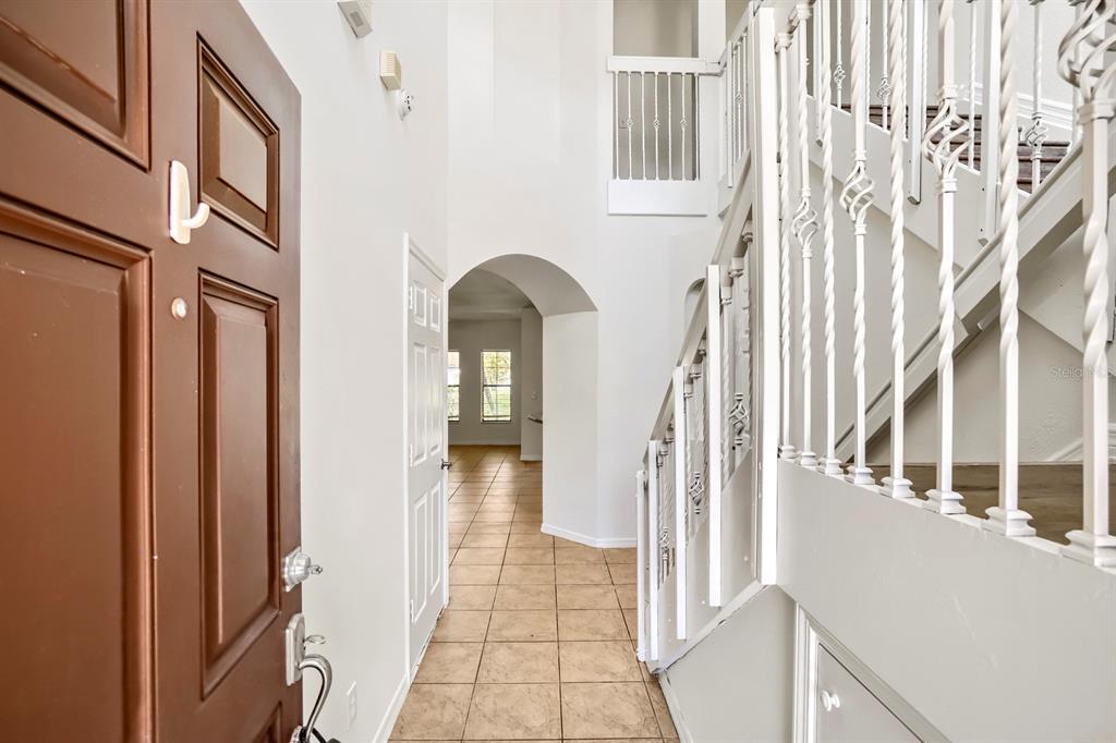 An entryway features a brown door, tile flooring, an arched doorway, and a white staircase — 1048 TULLAMORE DRIVE, WESLEY CHAPEL, FL