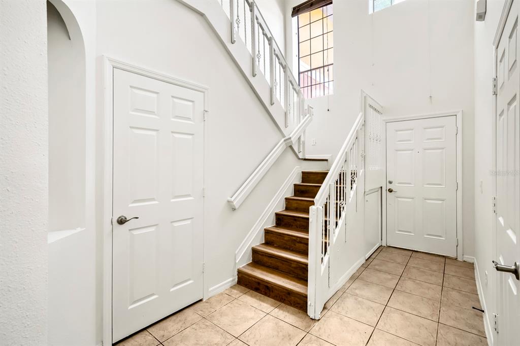 An entryway features a wooden staircase, white doors, and light-colored tile flooring — 1048 TULLAMORE DRIVE, WESLEY CHAPEL, FL