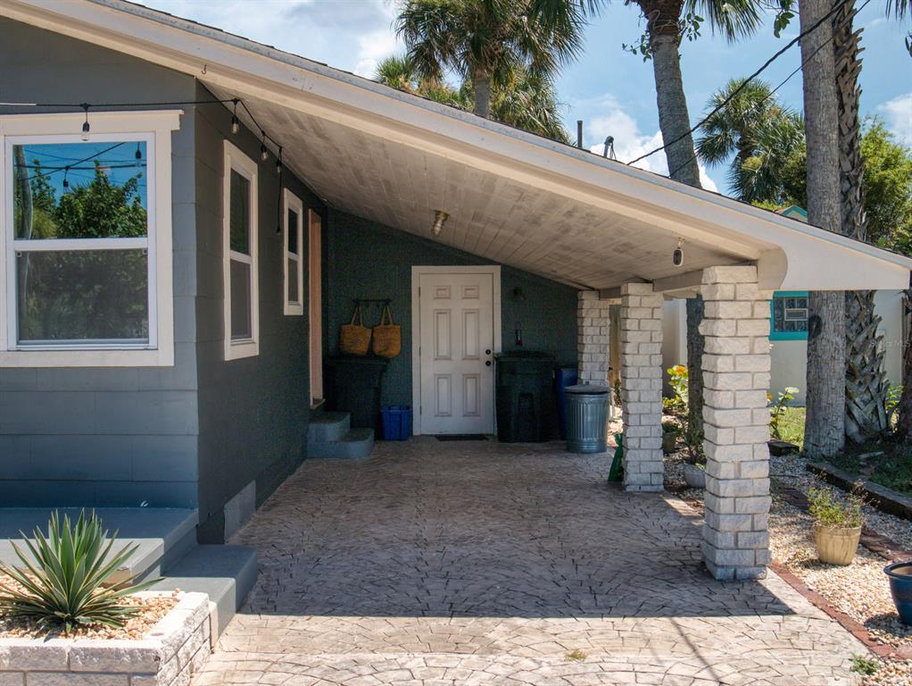 A gray house features a covered carport with stone pillars and a stamped concrete driveway — 207 Kirkland ROAD, NEW SMYRNA BEACH, FL