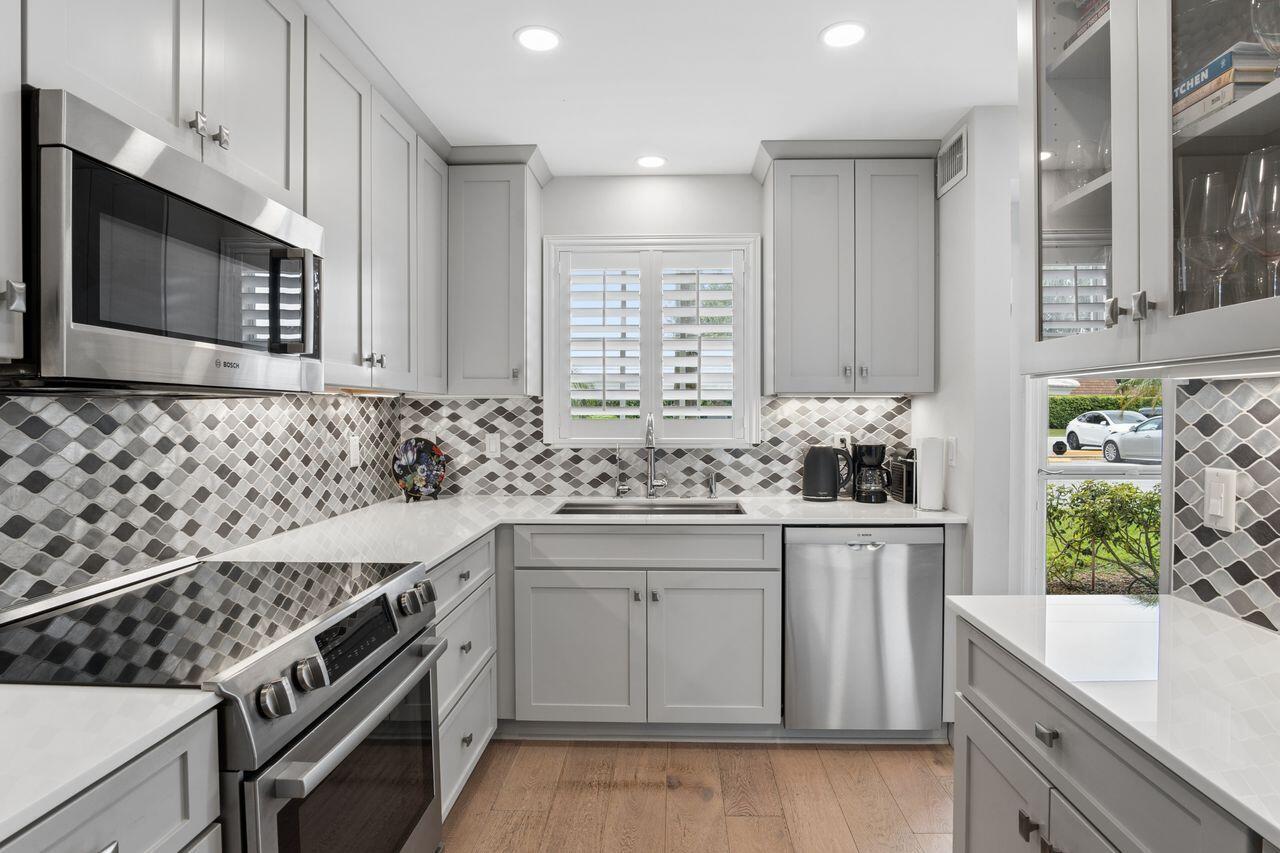 A modern kitchen features white cabinetry, stainless steel appliances, and a patterned tile backsplash — 157 Atlantis Boulevard # 103, Atlantis FL 33462, ATLANTIS, FL