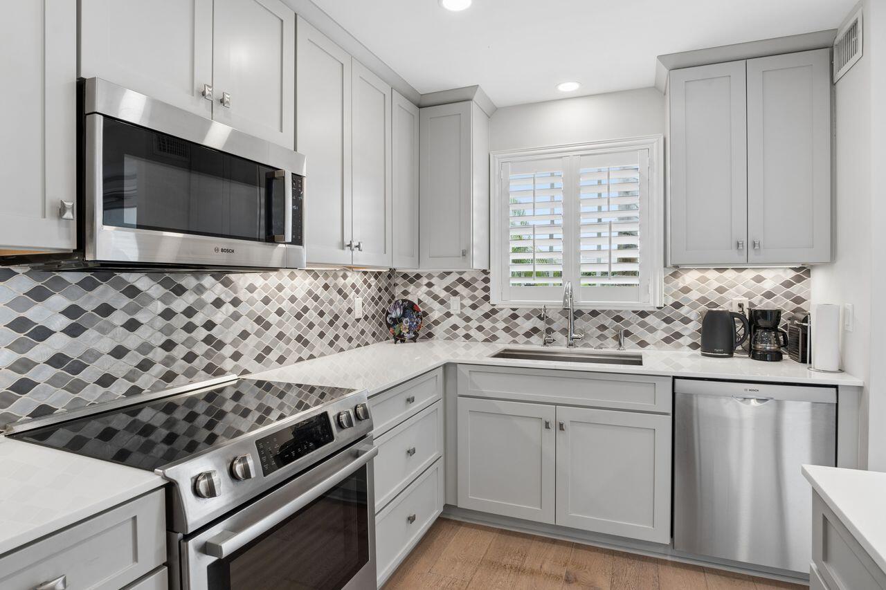 A kitchen with gray cabinets, stainless steel appliances, a patterned backsplash, and a window — 157 Atlantis Boulevard # 103, Atlantis FL 33462, ATLANTIS, FL