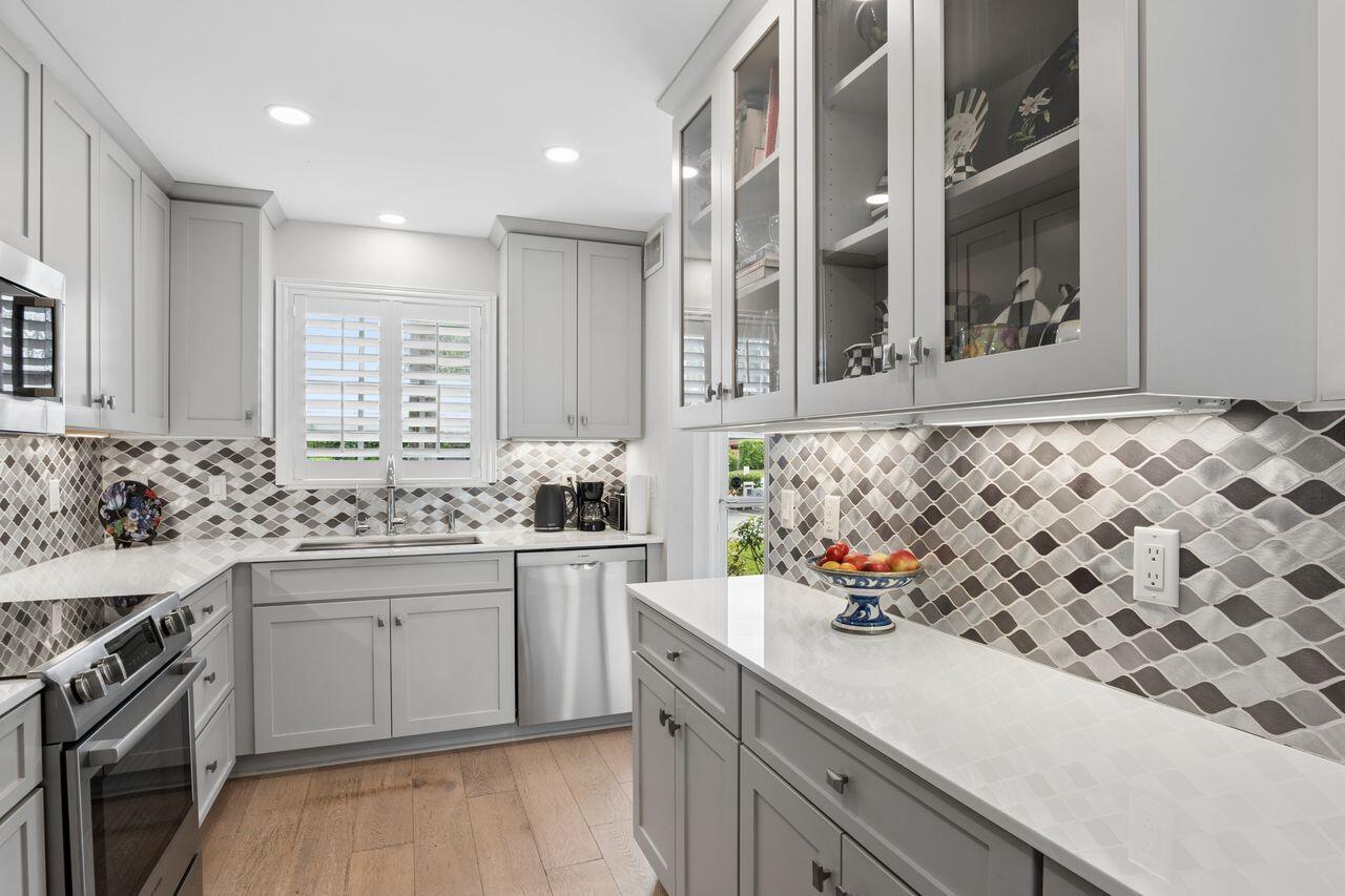 A modern kitchen features light gray cabinets, stainless steel appliances, and a patterned tile backsplash — 157 Atlantis Boulevard # 103, Atlantis FL 33462, ATLANTIS, FL