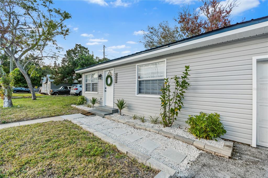 A light gray house exterior features a white front door, windows, and a stone walkway — 7799 46TH AVE N, ST PETERSBURG, FL