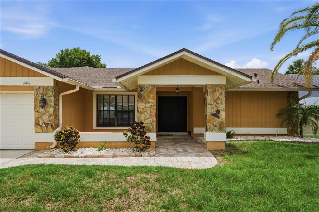 A single-story house with tan siding, stone pillars, and a paved walkway leading to the entrance — 11803 SWEETPEA COURT, TAMPA, FL
