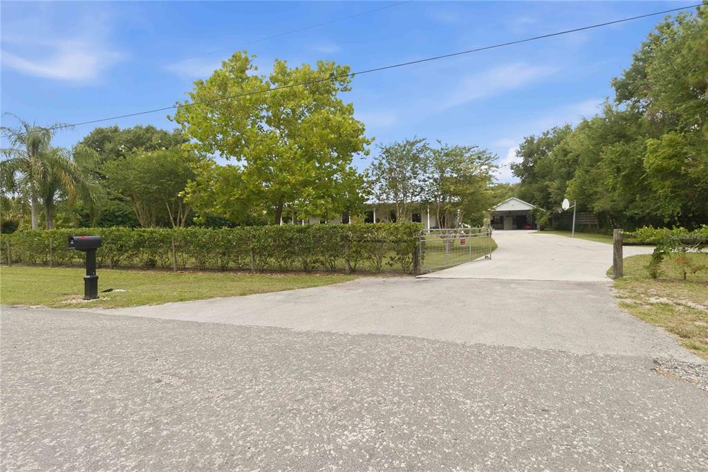 A paved driveway leads to a house partially obscured by trees behind a hedge fence — 3050 S INDIANA AVENUE, ST CLOUD, FL
