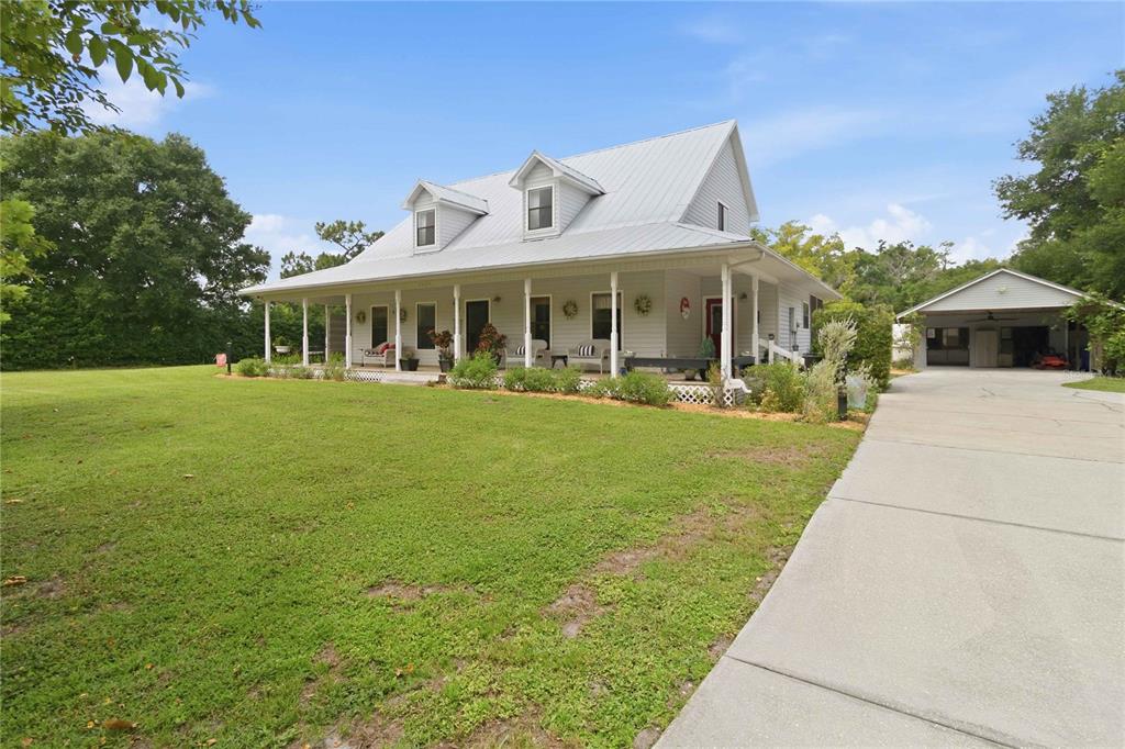 A white farmhouse with a metal roof, front porch, and detached carport sits on grass — 3050 S INDIANA AVENUE, ST CLOUD, FL