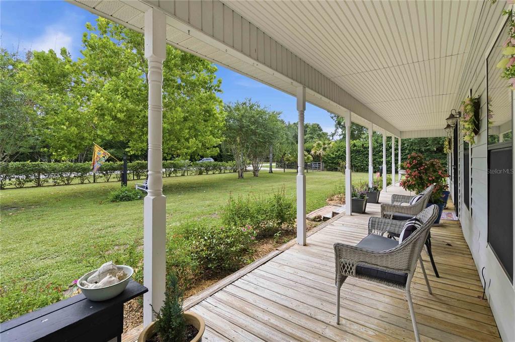 A covered wooden porch features white columns, wicker chairs, and a view of a grassy yard — 3050 S INDIANA AVENUE, ST CLOUD, FL