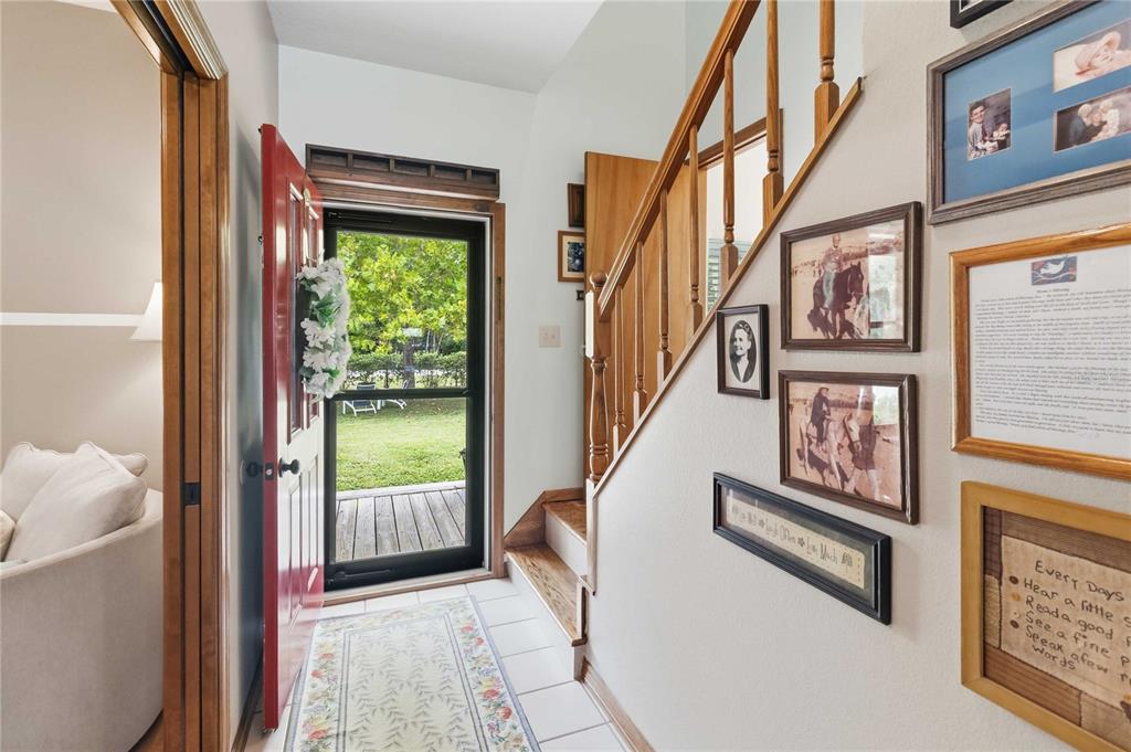 An entryway features a red front door, tiled floor, wooden staircase, and a gallery wall — 3050 S INDIANA AVENUE, ST CLOUD, FL