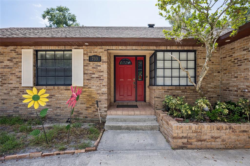 A brick house exterior features a red front door, a large window, and garden decor — 733 SAXBY AVENUE, ORLANDO, FL