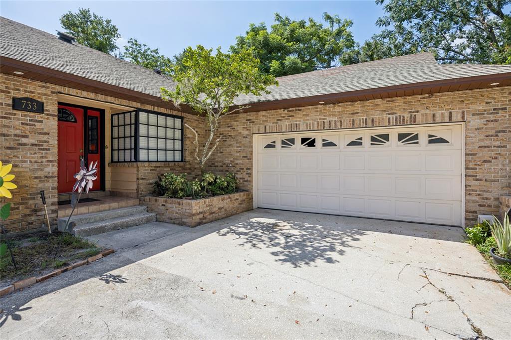 A brick house exterior features a red front door, a garage, and a small garden — 733 SAXBY AVENUE, ORLANDO, FL