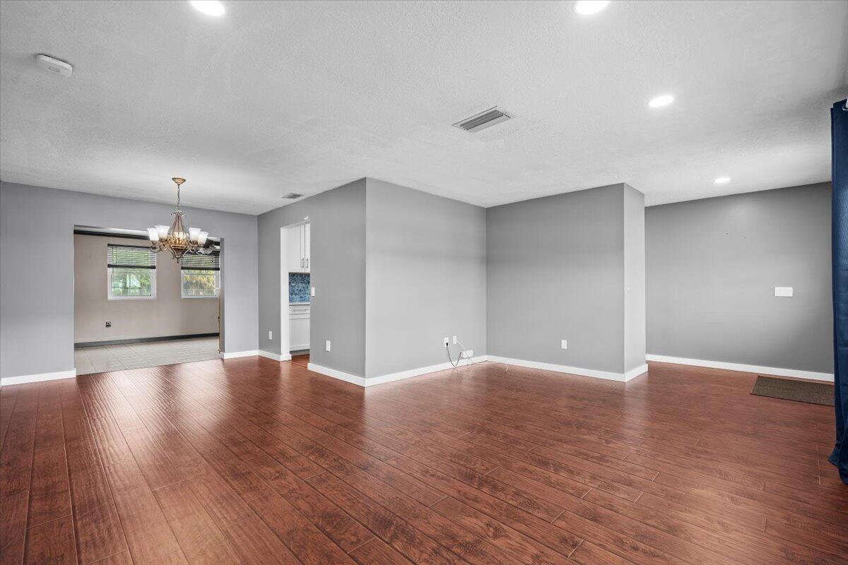 An empty room with gray walls and dark wood-look flooring features a chandelier and recessed lighting — 7423 Oakmont Drive, FL 33467, FL