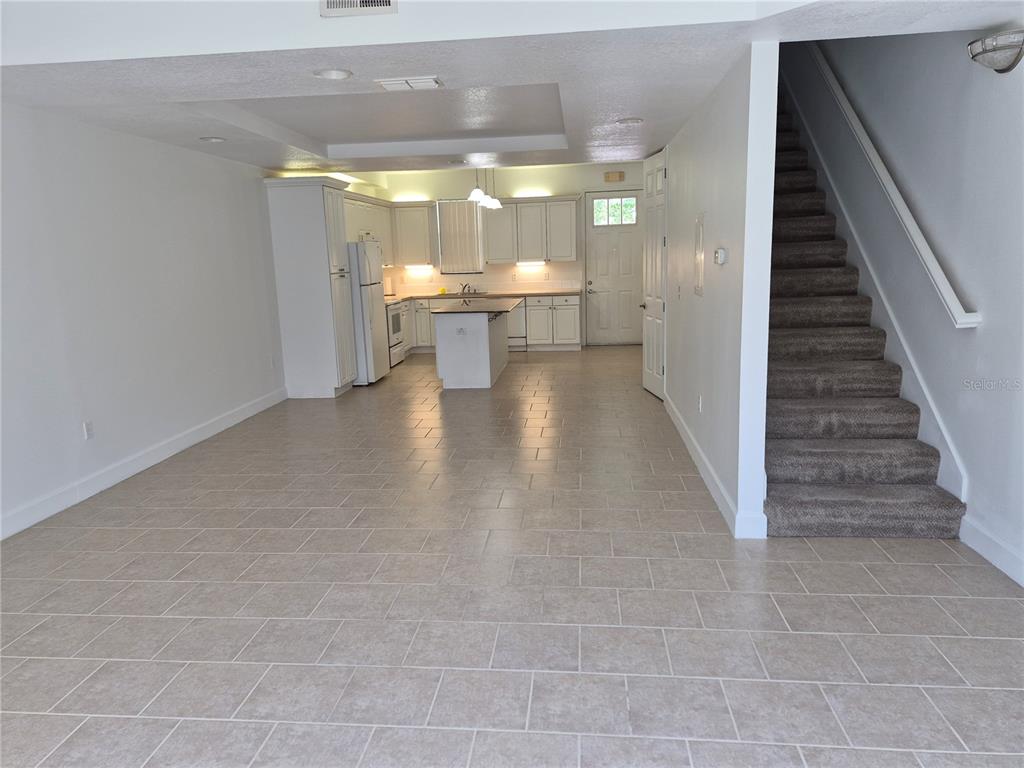 An open-concept kitchen with white cabinetry and tile flooring sits adjacent to a carpeted staircase — 2080 HERITAGE KEY BOULEVARD, KISSIMMEE, FL