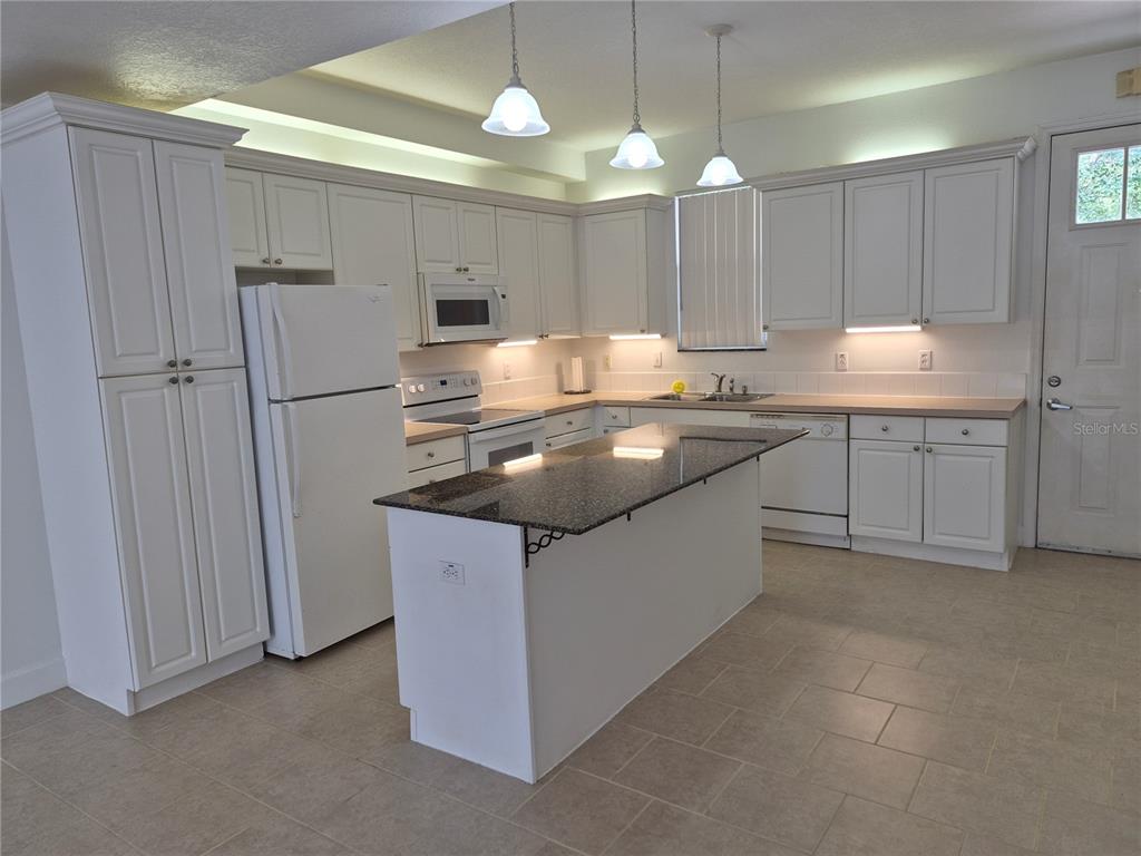 A kitchen features white cabinets, a dark granite island, and light tile flooring — 2080 HERITAGE KEY BOULEVARD, KISSIMMEE, FL