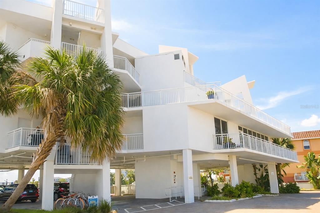 A multi-story white apartment building with elevated parking and balconies under a blue sky — 10091 GULF BOULEVARD UNIT 202E, TREASURE ISLAND, FL