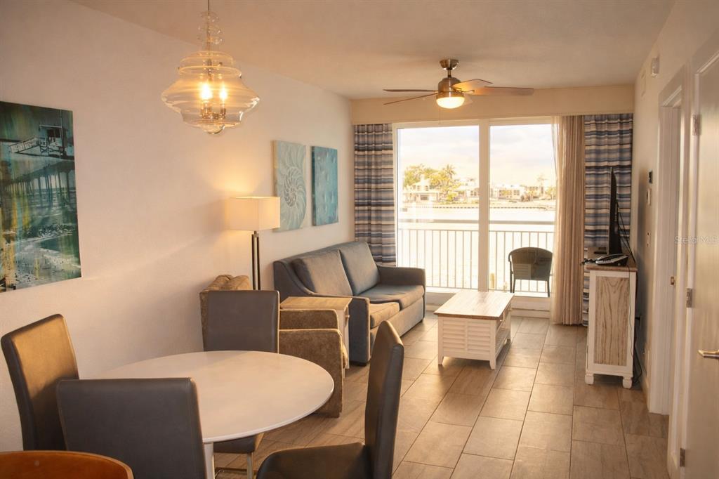 A living and dining area with tile floors, a sofa, and a balcony view — 10091 GULF BOULEVARD UNIT 202E, TREASURE ISLAND, FL