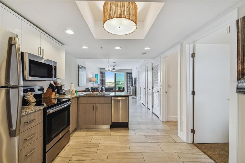 A modern kitchen with stainless steel appliances and wood cabinets opens into a living area — 10091 GULF BOULEVARD UNIT 202E, TREASURE ISLAND, FL
