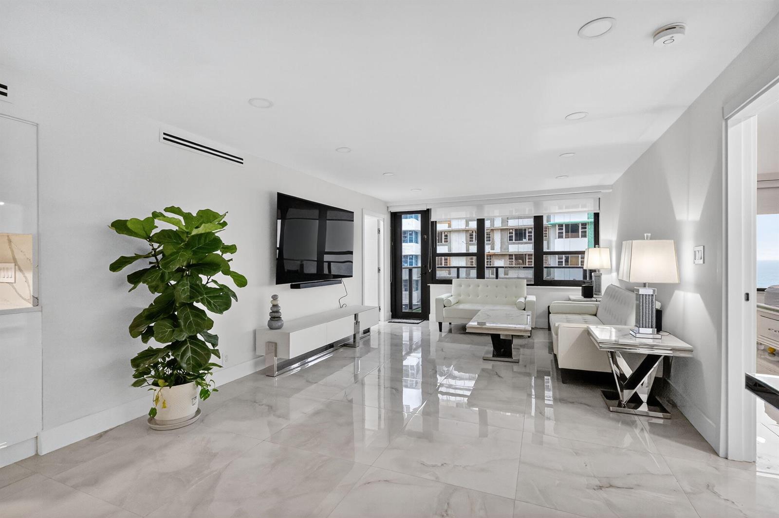 A modern living room features white tile floors, a wall-mounted television, and white leather furniture — 5225 Collins Avenue # 1408, Miami Beach FL 33140, MIAMI BEACH, FL
