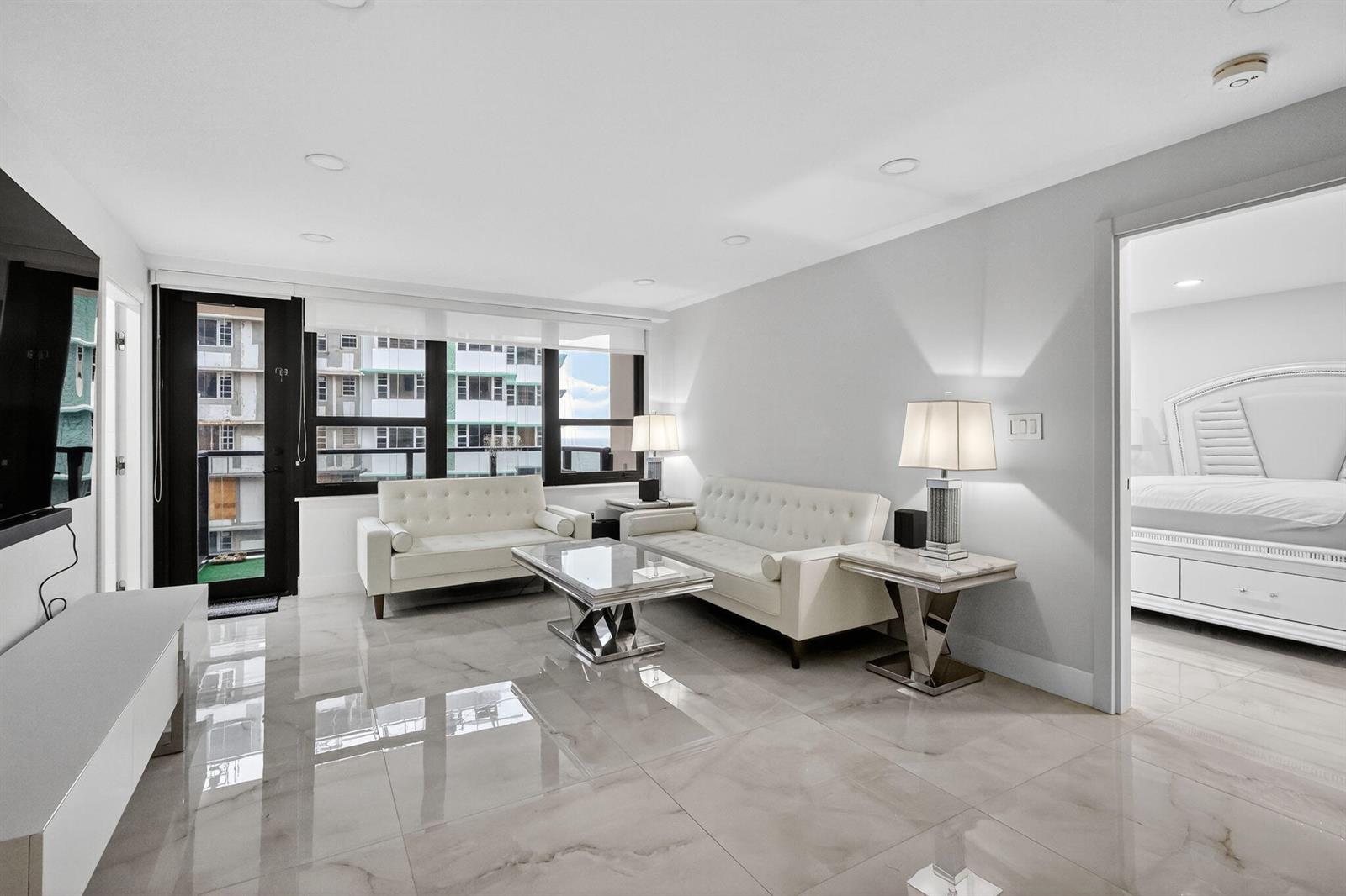 A modern living room with white tufted sofas, marble-style tile flooring, and an adjacent bedroom — 5225 Collins Avenue # 1408, Miami Beach FL 33140, MIAMI BEACH, FL