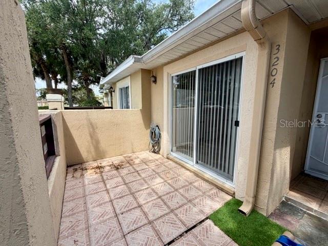A patio with tiled flooring, a sliding glass door, and a beige stucco wall — 3204 CRANES NEST LANE, KISSIMMEE, FL