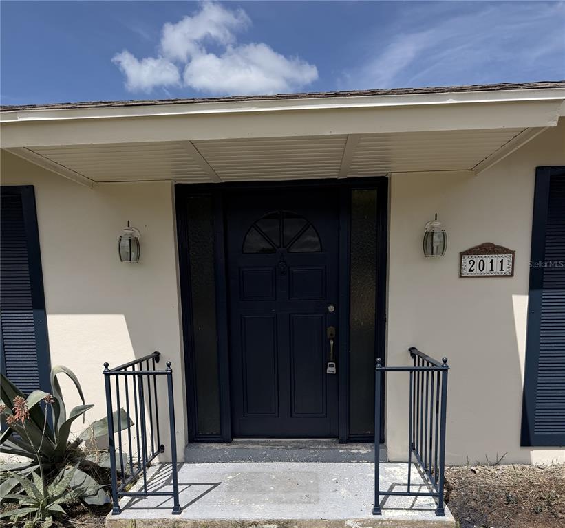 A single-story house exterior features beige stucco walls, dark blue shutters, and a dark roof — 2011 KEYES LANE, DELTONA, FL