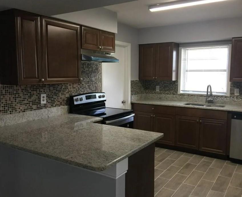 A kitchen features dark wood cabinets, granite countertops, a mosaic tile backsplash, and tile flooring — 2011 KEYES LANE, DELTONA, FL
