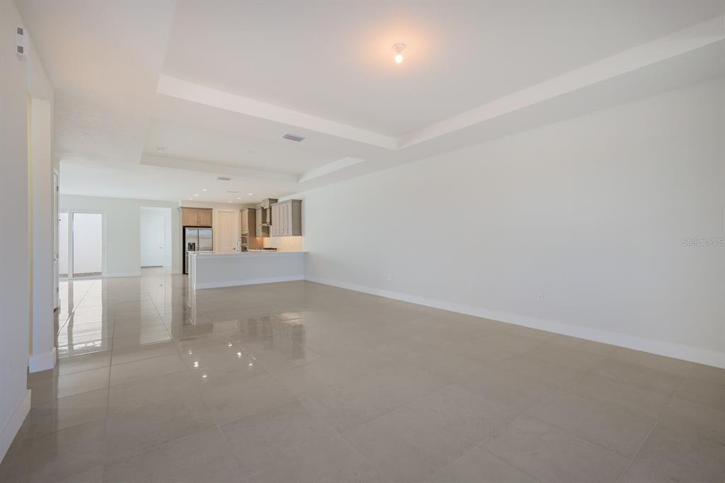 An open-concept living area features large light-colored floor tiles and a tray ceiling — 6009 WHITE MANGROVE LANE, BRADENTON, FL