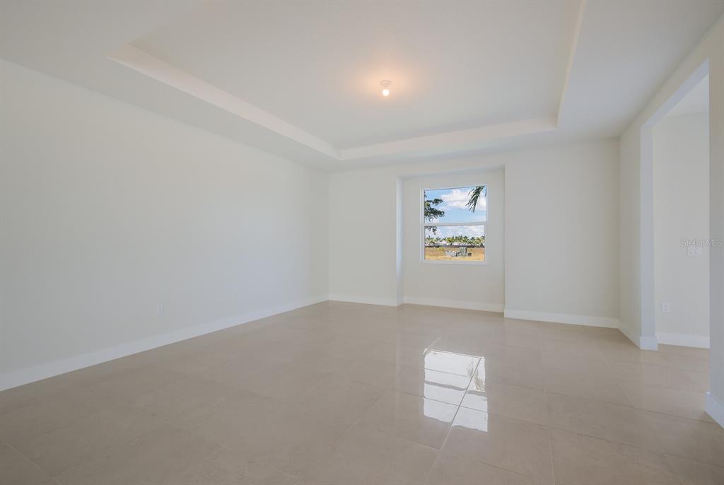 An empty room with light-colored tile flooring, white walls, and a recessed tray ceiling — 6009 WHITE MANGROVE LANE, BRADENTON, FL