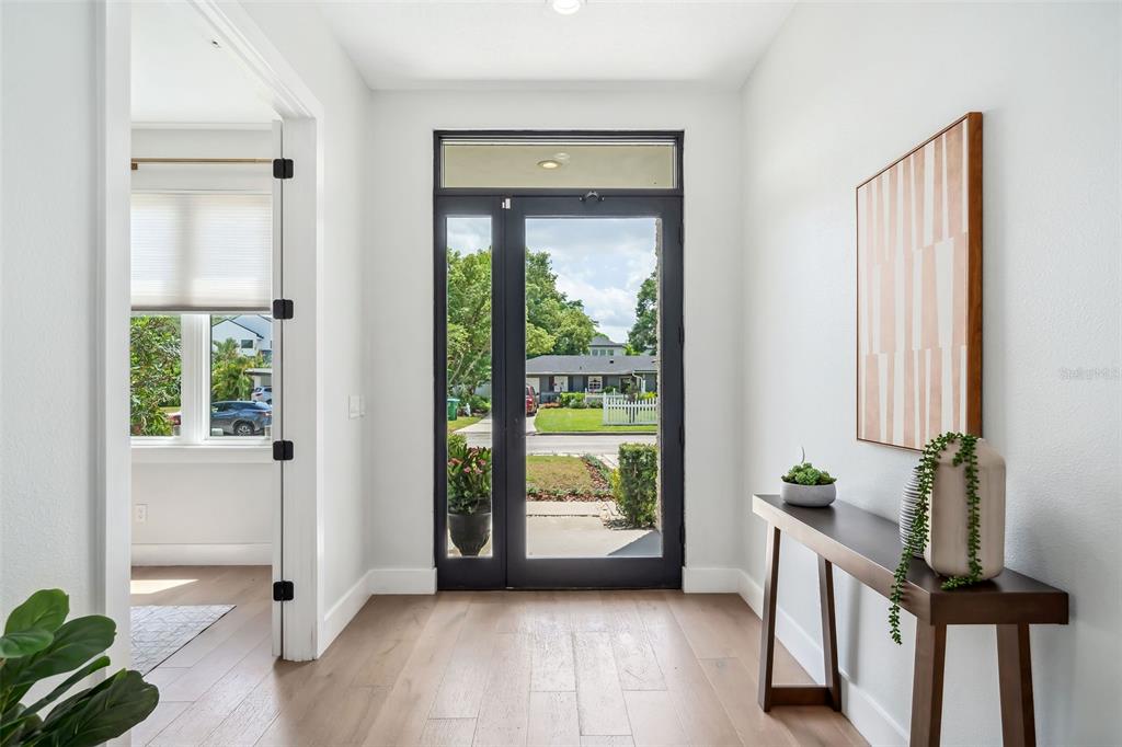 A bright entryway features light wood flooring, a dark-framed glass door, and a console table — 2407 LAFAYETTE AVENUE, WINTER PARK, FL