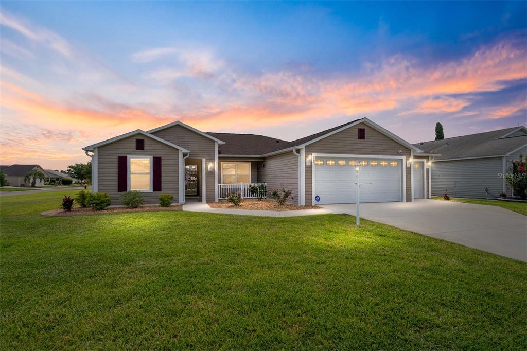 A single-story house with tan siding, a white garage door, and a green lawn — 2446 HOPESPRING LOOP, THE VILLAGES, FL