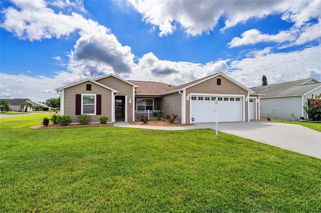 A single-story house with tan siding, a white garage door, and a green lawn — 2446 HOPESPRING LOOP, THE VILLAGES, FL